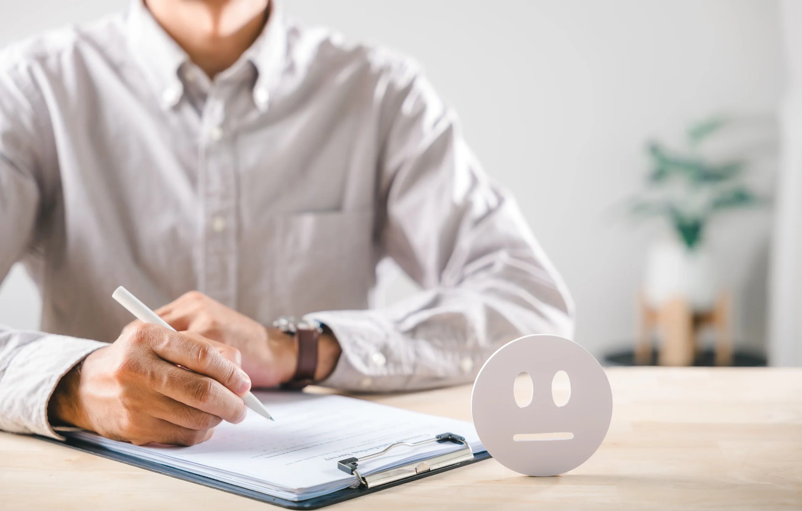 Man filling out forms beside a neutral-face figure, symbolizing the emotional strain assessed in a psychological evaluation