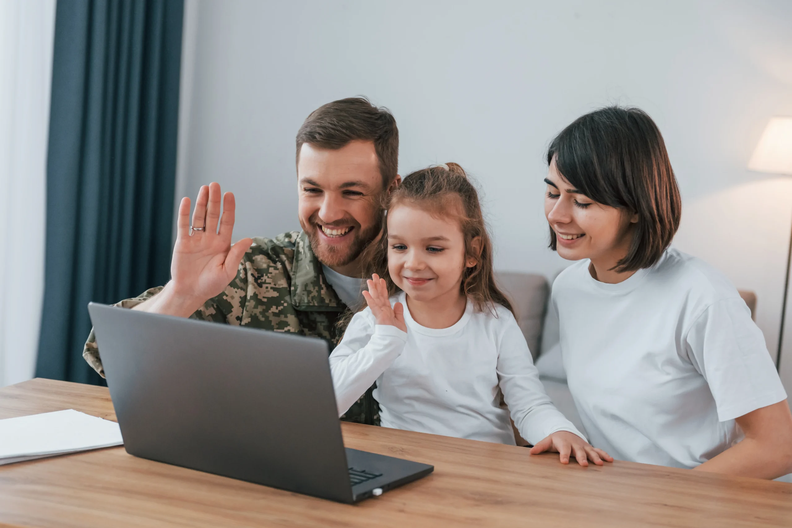 Family waving at a laptop while joining a secure video interview for a hardship evaluation