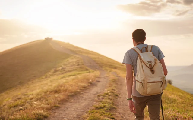 Man with a backpack walking up a sunlit path, symbolizing recovery for trafficking survivors applying for a T visa