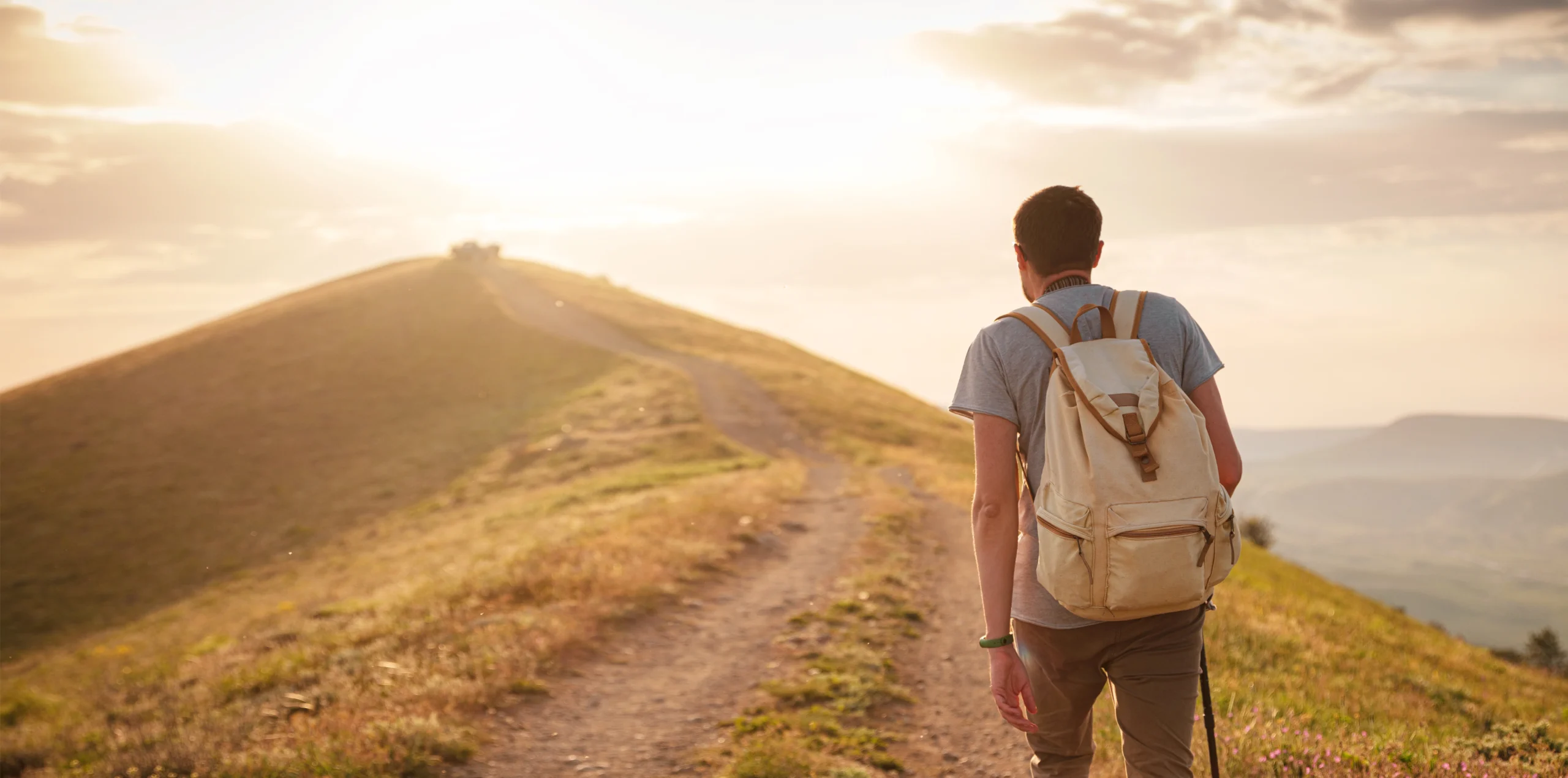 Man with a backpack walking up a sunlit path, symbolizing recovery for trafficking survivors applying for a T visa