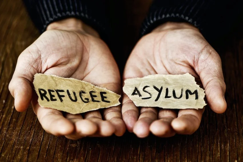 Open hands holding paper scraps with the words refugee and asylum, illustrating who is eligible for asylum protection