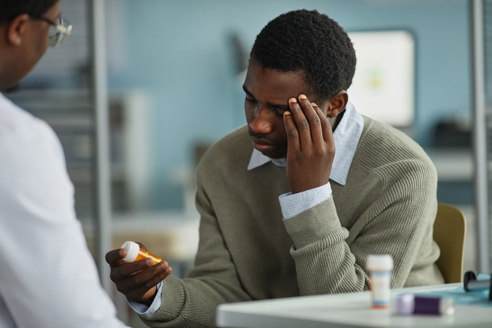 Young man looking at his prescription bottle while discussing medication side effects with a psychiatric provider