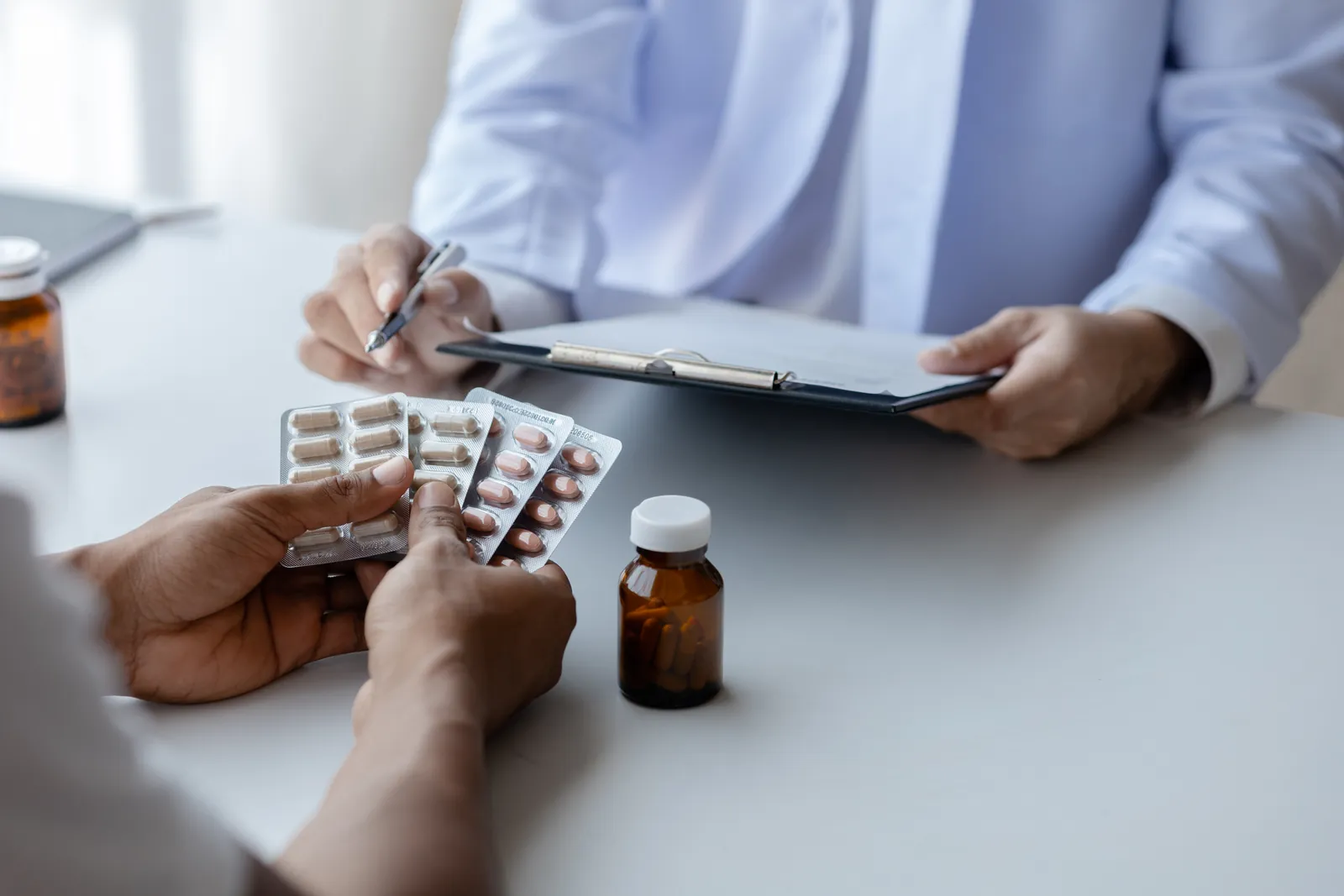 Patient holding blister packs of medication as a provider takes notes during a psychiatric medication consultation