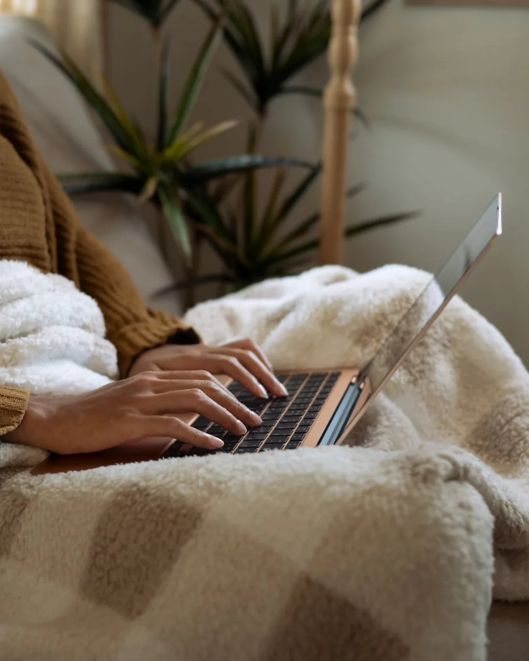 Person under a cozy blanket typing on a laptop at home, ready to schedule a confidential online psychiatric evaluation